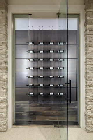 Glass and cable wine racks mounted floor to ceiling inside a glass and stone wine cellar