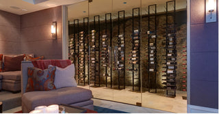 Several black floor to ceiling wine racks mounted side by side inside a glass and stone wine cellar